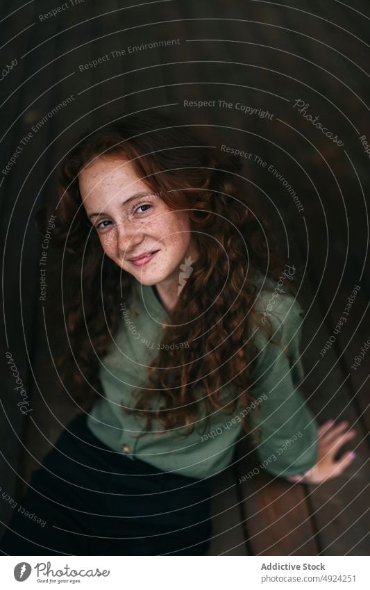 Happy redhead female sitting on floor and smiling woman smile portrait positive confident red hair freckle style glad curly hair individuality content long hair