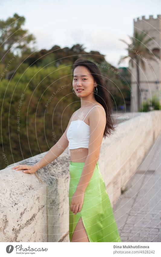 Beautiful young Asian woman walking the street of historic European town with palm trees. Female tourist from China traveling in Europe, smiling. Exchange student.