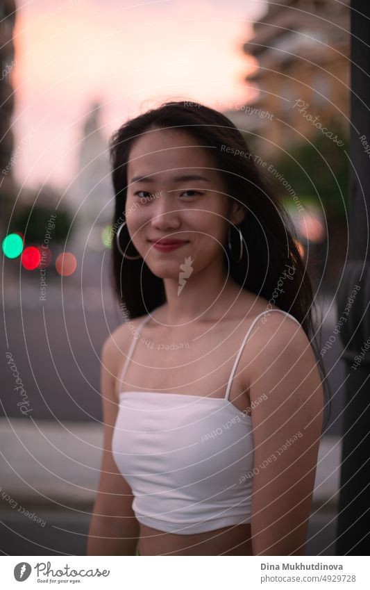 Beautiful young Asian woman walking the street of modern city at sunset closeup. Female tourist from China traveling in Europe. Fashion and style concept.