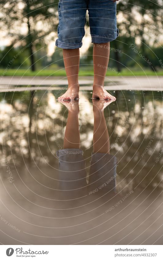 Boy in short jeans stands barefoot in rain puddle on playground Rain Rain puddle Puddle Water Surface of water Rainwater Water reflection Boy (child) Child