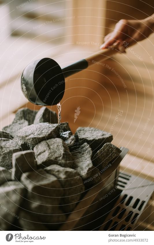 Hand of young woman pouring water on hot rocks in the sauna activity adult bath bathhouse bench body caucasian comfortable female health healthy heat heater