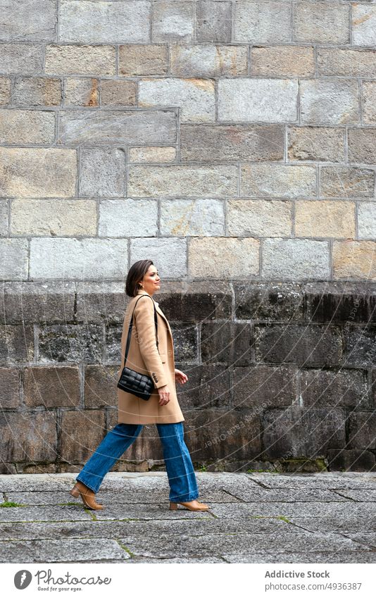 Stylish woman walking on street pavement house old smart casual female style building urban pedestrian sidewalk brunette aged town stroll structure autumn coat