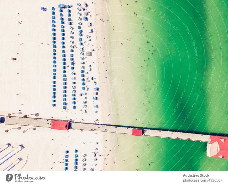 Long pier in clear sea with sandy coastline on sunny day ocean beach seashore resort sunbed umbrella seascape landscape nature scenic picturesque sunlight