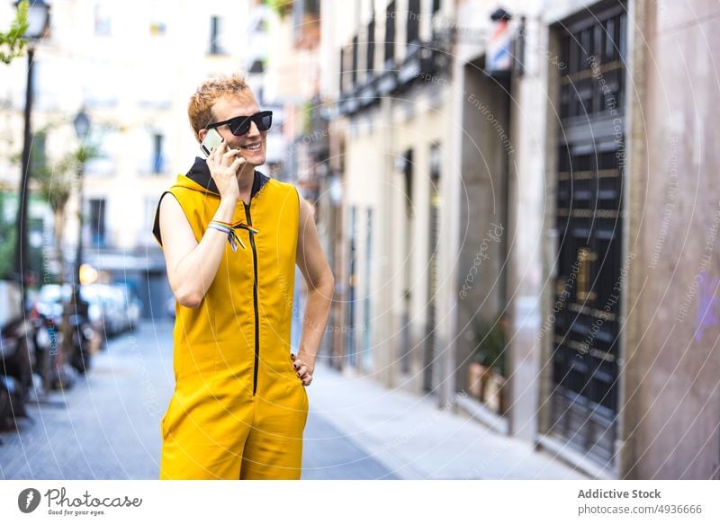 Smiling stylish non binary male speaking on smartphone on street man style urban cheerful delight talk transgender phone call confident modern lgbt walk young