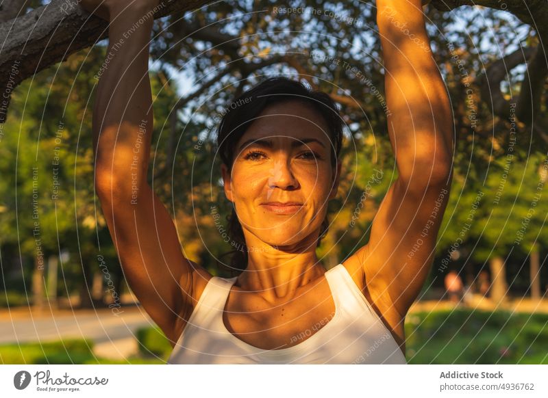 Happy woman hanging on tree branch training sport workout park fitness healthy lifestyle positive friendly cheerful content hobby happy smile delight plant