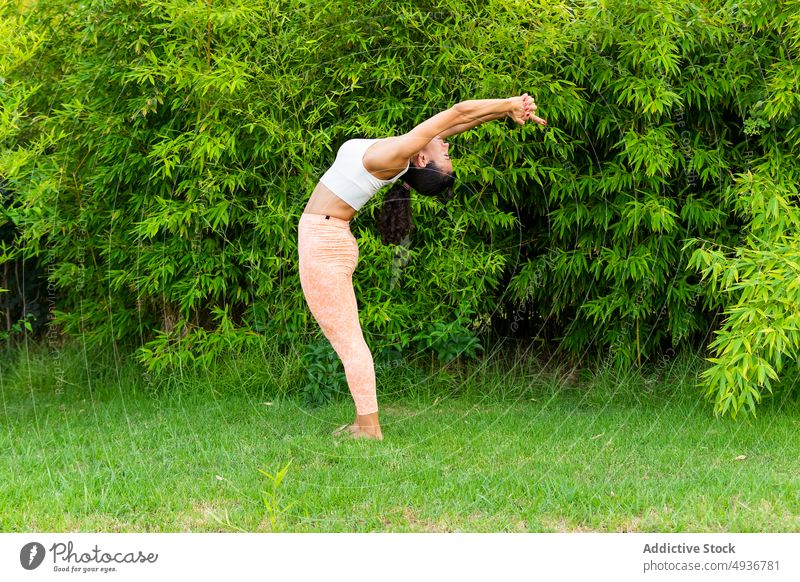 Woman doing Mountain asana with arms up and backbend woman yoga mountain pose arms raised park training exercise practice ardha chandrasana tree shape lawn zen