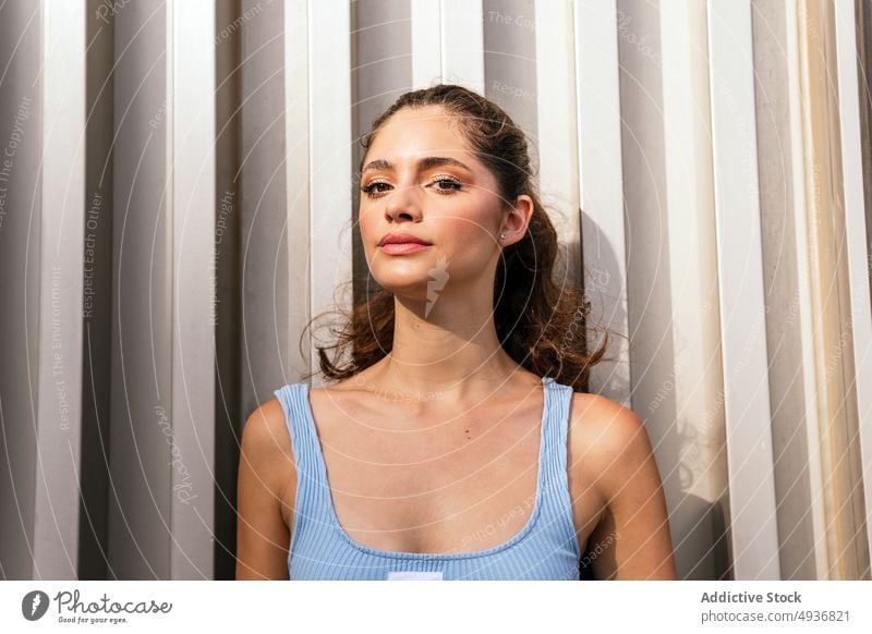 Cool young woman standing near wall on street in sunlight self assured confident style appearance portrait personality millennial cool charismatic feminine