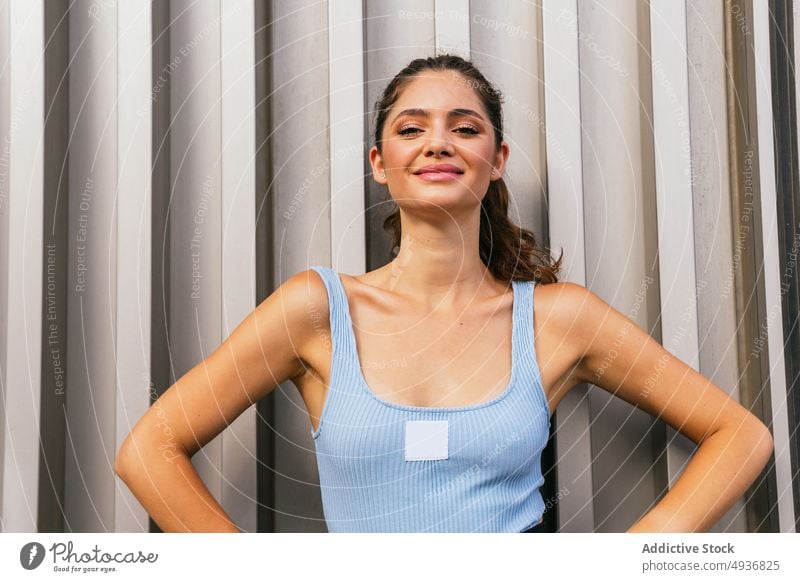 Smiling young woman standing near wall on street in sunlight self assured confident style appearance portrait personality millennial cool charismatic feminine