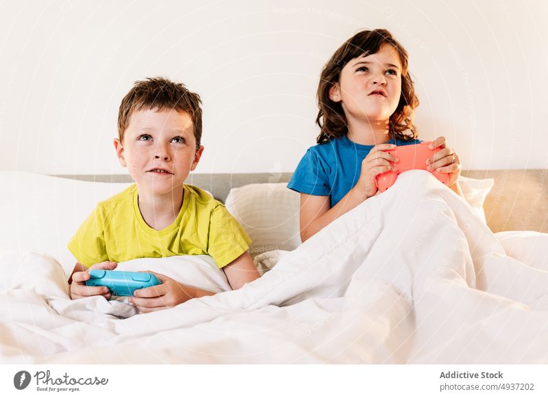 Children playing video game in bed children sibling gamepad videogame entertain amusement pastime leisure hobby focused sister concentrated brother boy girl