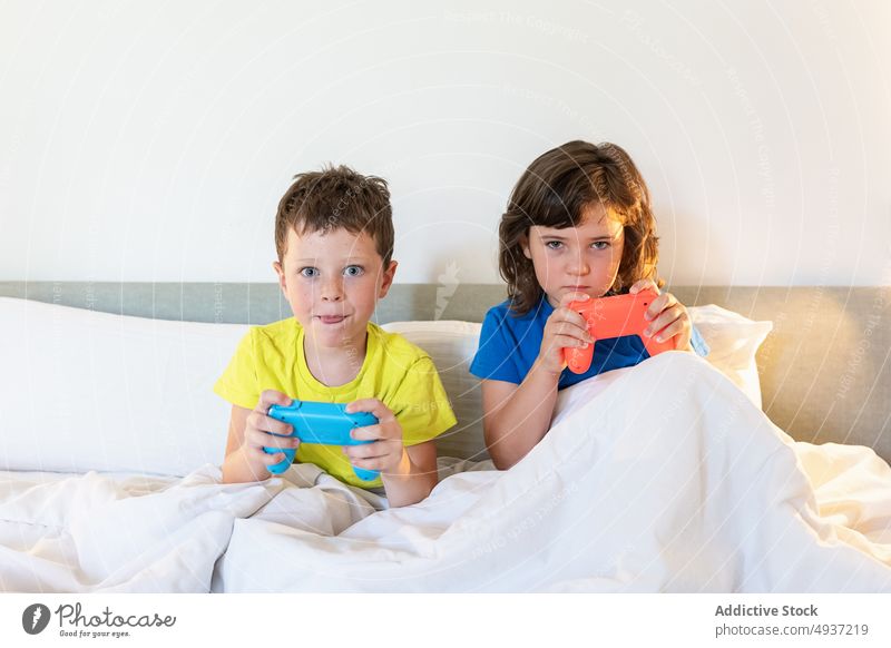 Children playing video game in bed children sibling gamepad videogame entertain amusement pastime leisure hobby focused sister concentrated brother boy girl