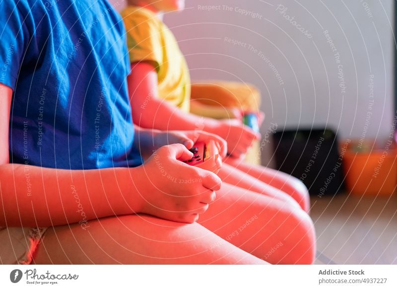 Anonymous children playing video game in evening time sibling living room videogame entertain amusement pastime leisure couch sofa dim neon late hobby hands