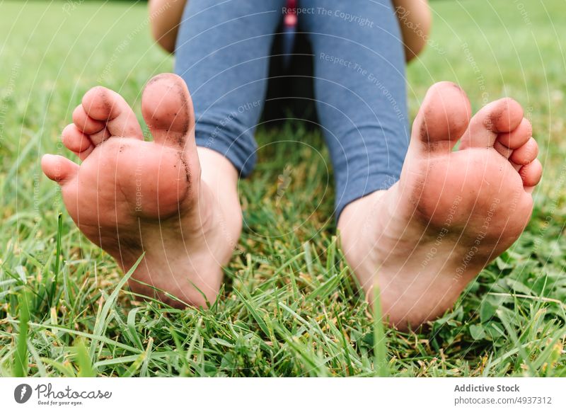 Crop child sitting on grass lawn summer park barefoot dirty leggings weekend fresh daytime free time kid green childhood pastime lush season soft delicate