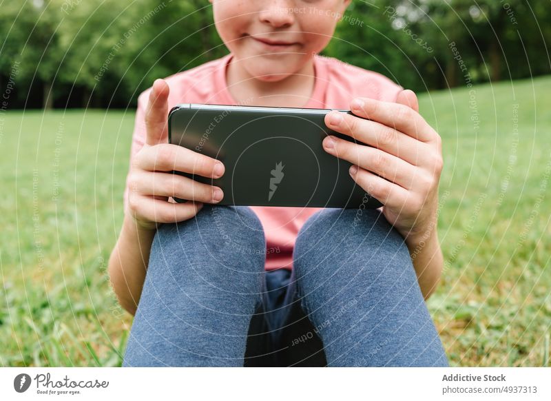 Happy boy using smartphone on park lawn watch video weekend summer pastime happy child gadget device cellphone delight grass glad internet childhood online kid