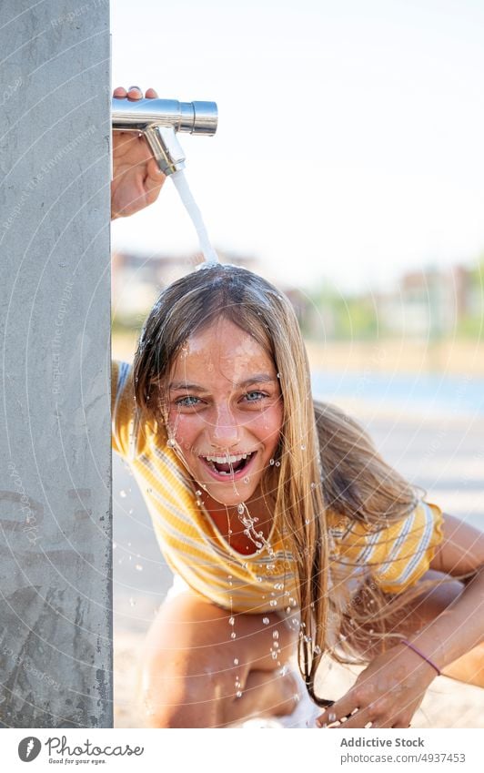 Happy girl standing under water on shore teenage carefree tap having fun waterfront embankment playful coast wet hair excited street stream summer content enjoy