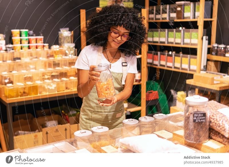 Friendly African American vendor with dried fruits woman smile show container zero waste store portrait female young black african american ethnic uniform