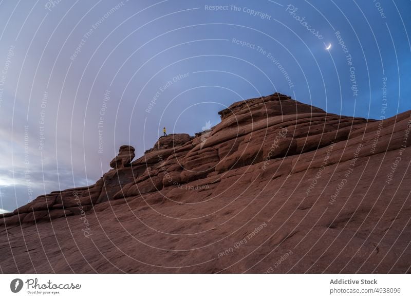 Traveler on top of rock formation against sky and moon tourist stone desert evening cliff nature trip landmark balanced rock arches national park moab utah usa