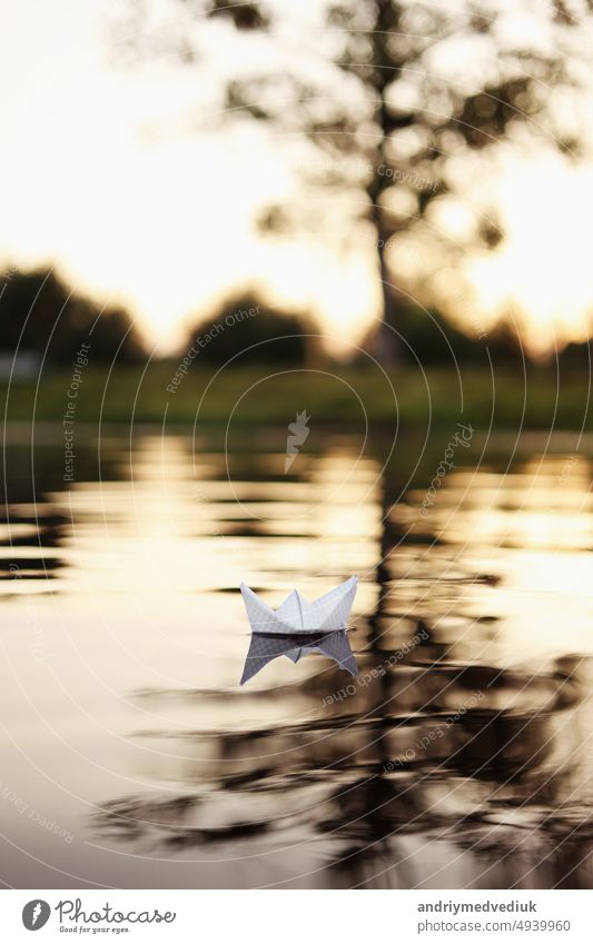 A paper boat is floating on the waves in the water at a beautiful sunset. Origami ship Sailing. The concept of a dream, future, childhood, freedom or hope. sea