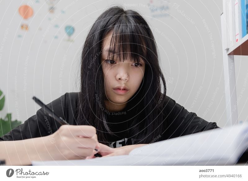 Asian student girl is writing homework and reading book at desk child person education school learn study female little paper elementary write crayons childhood