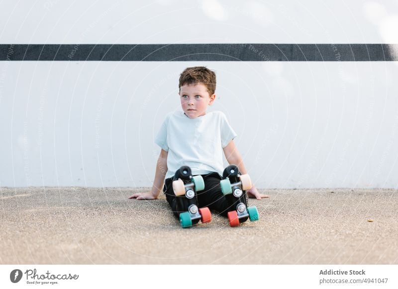 Boy in roller skates sitting on ground boy break street wall hobby summer activity kid casual rest child relax daytime childhood generation construction pastime