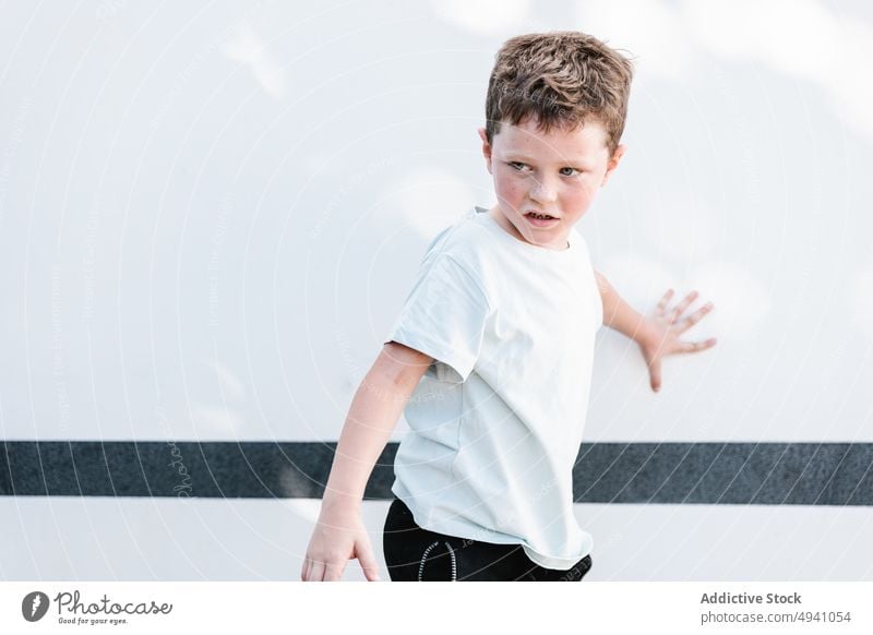 Boy standing against white wall boy street sunlit weekend appearance daytime summer urban modern kid casual sunlight daylight stripe child building t shirt