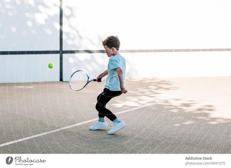 Boy learning to play tennis on street boy hit racket ball player summer weekend daytime kid game child activity hobby challenge casual recreation skill practice