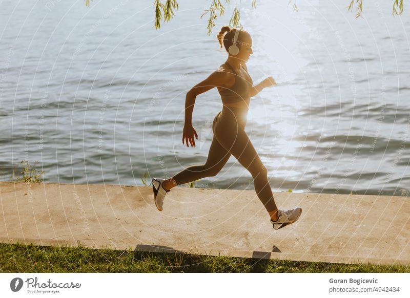 Active young beautiful woman running on the promenade along the riverside active activity athlete athletic city endurance exercise female fitness headphone