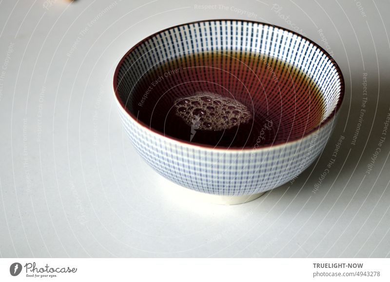 Tea bowl fine blue and white patterned in Japanese Tokusa design with freshly brewed Assam organic black tea on which some air bubbles float Black tea