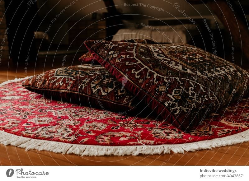 Two red persian bed pillows on a round hand knitted rug on the floor. Home decoration detail, copy space. Colorful carpet and textile. antique arabic asian