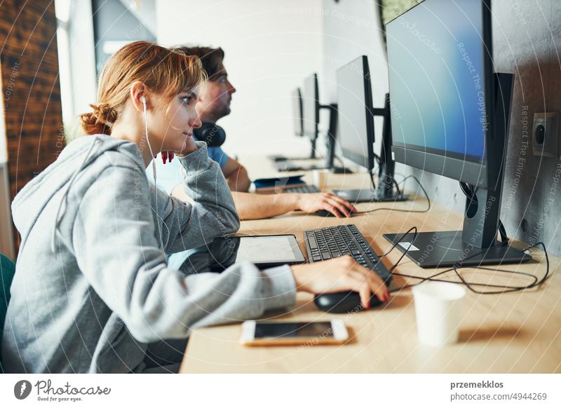 Students learning in computer classroom. Young man preparing for test on computer. Girl writing essay and making notes using computer. Focused students studying for college exams