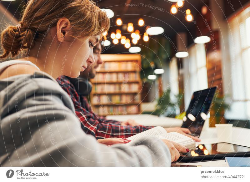 Students learning in university library. Young man preparing for test on laptop. Girl learning from book. Focused students studying for college exams Students discussing and learning together