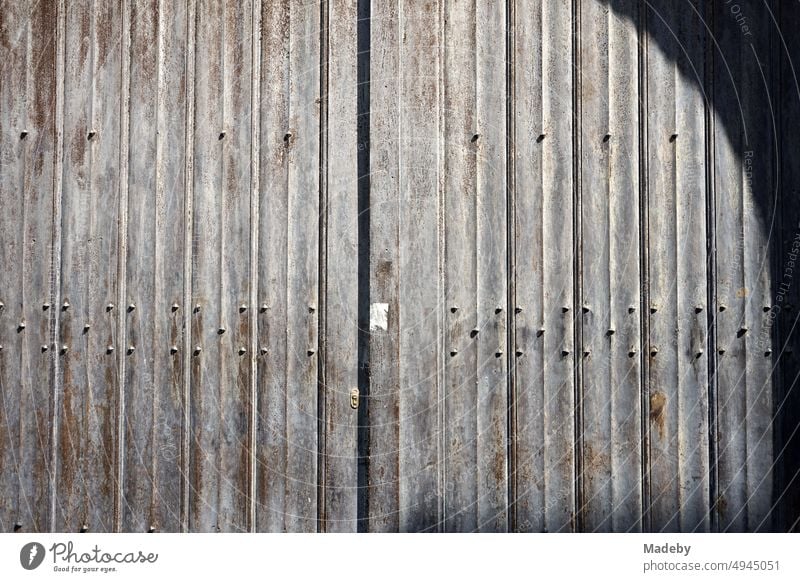 Old gray steel gate with texture, rust, patina and shadow of a round arch in the sunshine in the alleys of the old town of Bruges in West Flanders in Belgium