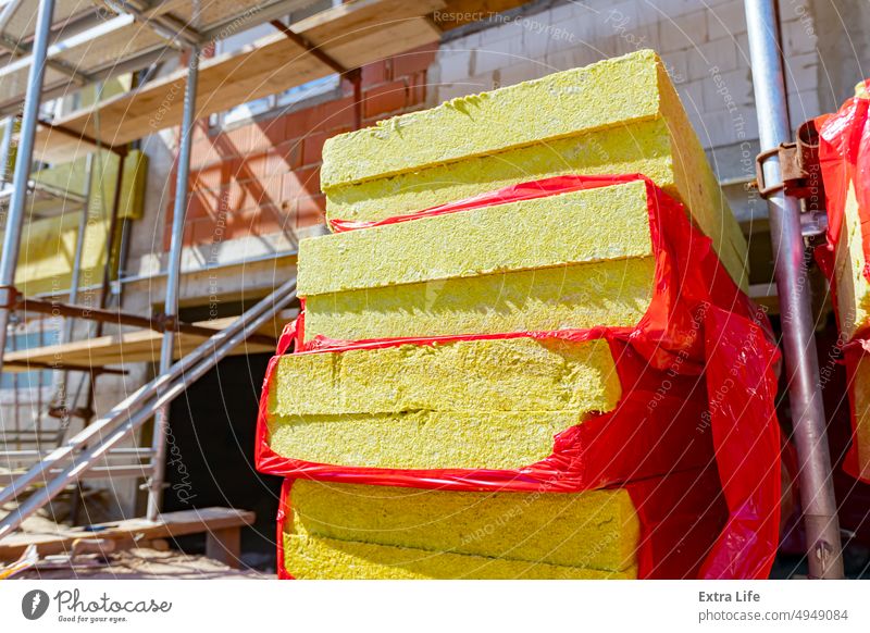 Stack of thermal insulation material is wrapped with cellophane foil. Unfinished edifice with scaffolding Bag Building Site Cellophane Civil Engineering