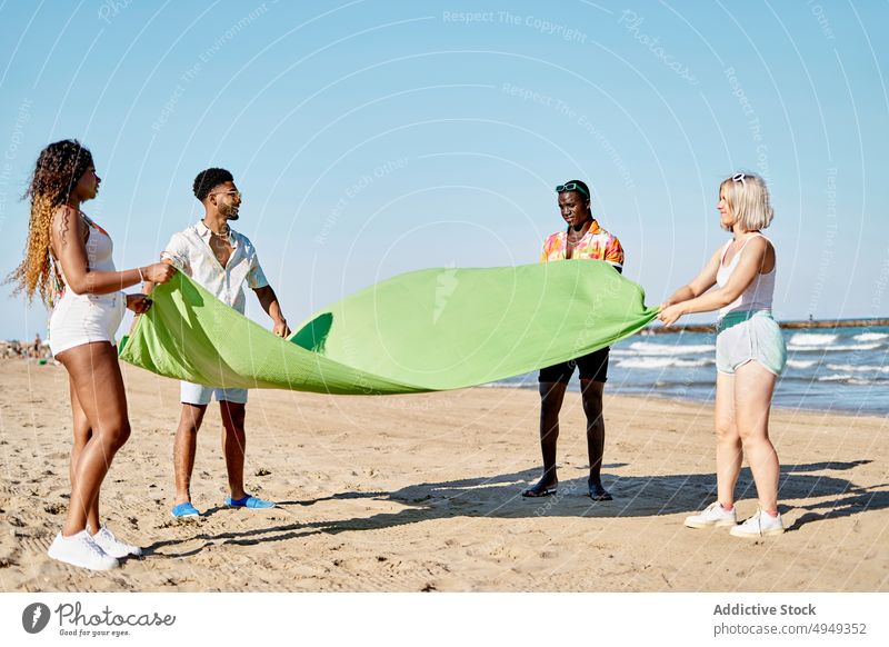 Diverse men and women laying blanket on beach friend sea weekend summer wave spread together girlfriend boyfriend relationship vacation coast casual resort