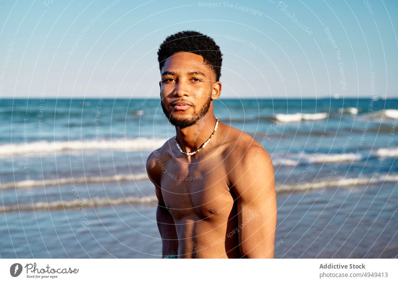 Black young male tourist standing near sea man beach summer weekend curly hair resort vacation thoughtful holiday portrait coast shore tourism activity water