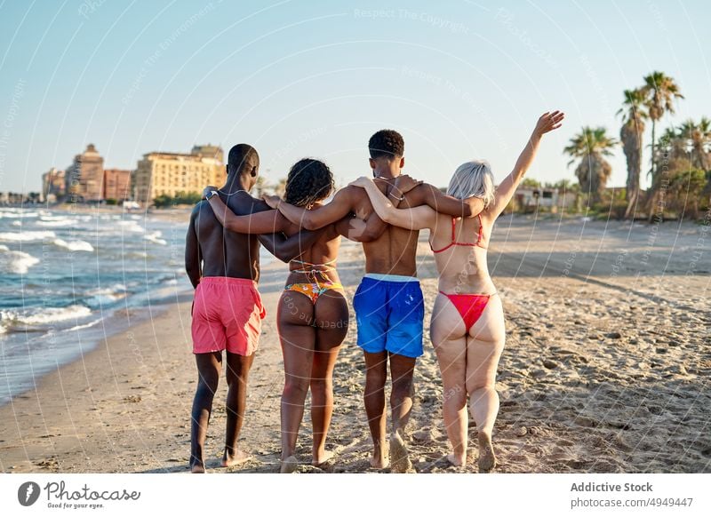 Anonymous merry diverse friends hugging on beach weekend summer walk together happy vacation resort men women embrace girlfriend boyfriend positive shore