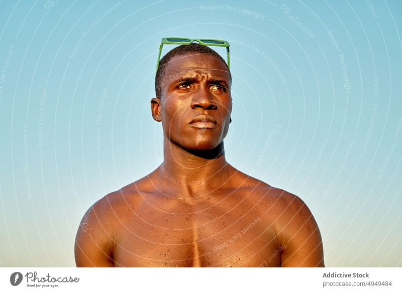 Serious black man near sea at sunset beach vacation serious weekend cloudless sky sunglasses portrait male african american ethnic shirtless summer calm sundown