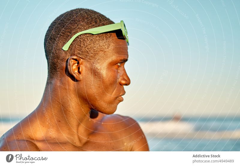 Serious black man near sea at sunset beach vacation serious weekend cloudless sky sunglasses portrait male african american ethnic shirtless summer calm sundown