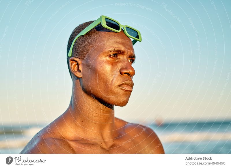 Serious black man near sea at sunset beach vacation serious weekend cloudless sky sunglasses portrait male african american ethnic shirtless summer calm sundown