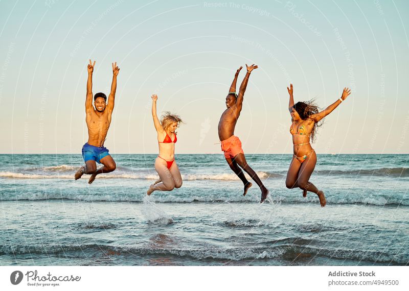 Diverse friends jumping in sea water wave sunset energy happy together weekend evening men women summer cheerful girlfriend boyfriend arms raised