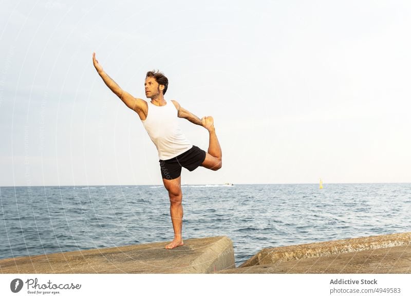 Mature male doing Natarajasan pose on embankment man yoga balance sea border Lord of the Dance Pose practice summer zen daytime wellbeing Natarajasana energy