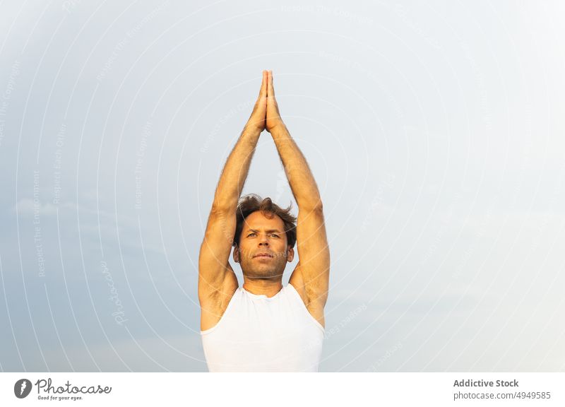 Mature male doing Vriksasana pose against gray sky man yoga practice balance tree pose summer zen daytime wellbeing energy arms raised wellness middle age