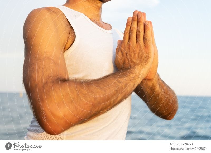 Crop male meditating with clasped hands near sea man meditate sunrise namaste morning session yoga practice mindfulness tank top hands clasped spirit wellness