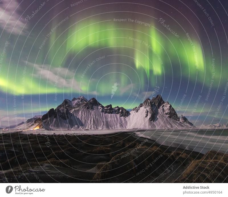 Water and snowy mountain against polar lights water sky aurora night peak shore winter calm vestrahorn iceland coast nature lake weather picturesque