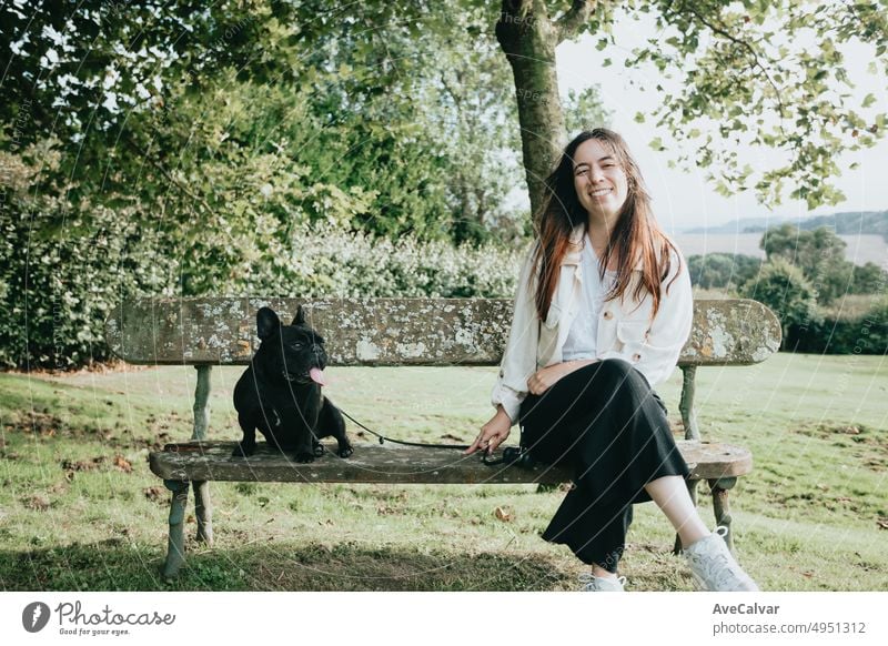 Young woman hugging cute dog in nature with copy space during a happy walking day. French bulldog pure breed dog. New member in the family owner pet person