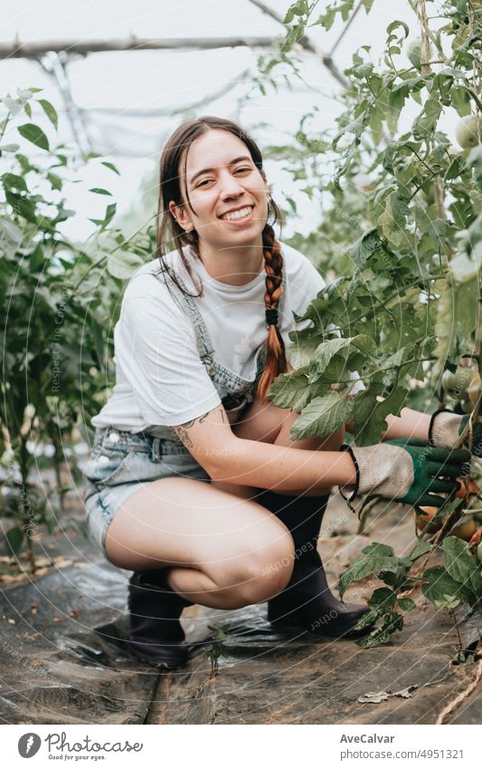 Portrait of a Happy and positive young adult woman working in greenhouse while using gloves to grow vegetables. Sustainability and healthy food concept. Bio eco. Organic raw products grown on a home farm