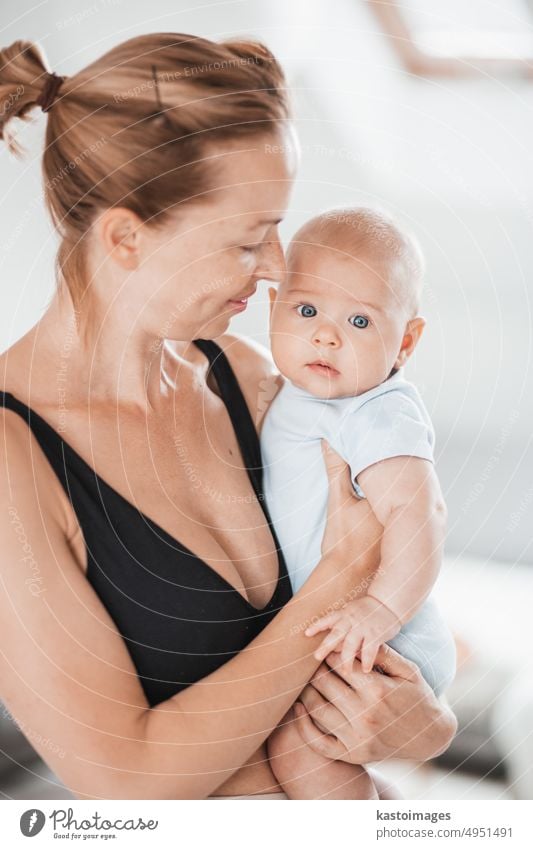 Portrait of sweet baby resting in mothers arms, looking at camera. New mom holding and cuddling little kid, embracing child with tenderness, love, care. Motherhood concept.