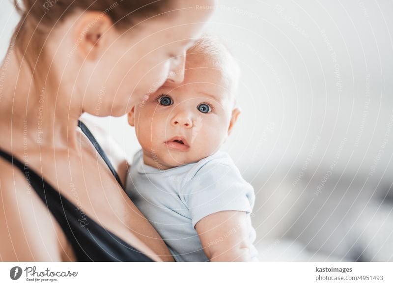 Portrait of sweet baby resting in mothers arms, looking at camera. New mom holding and cuddling little kid, embracing child with tenderness, love, care. Motherhood concept.