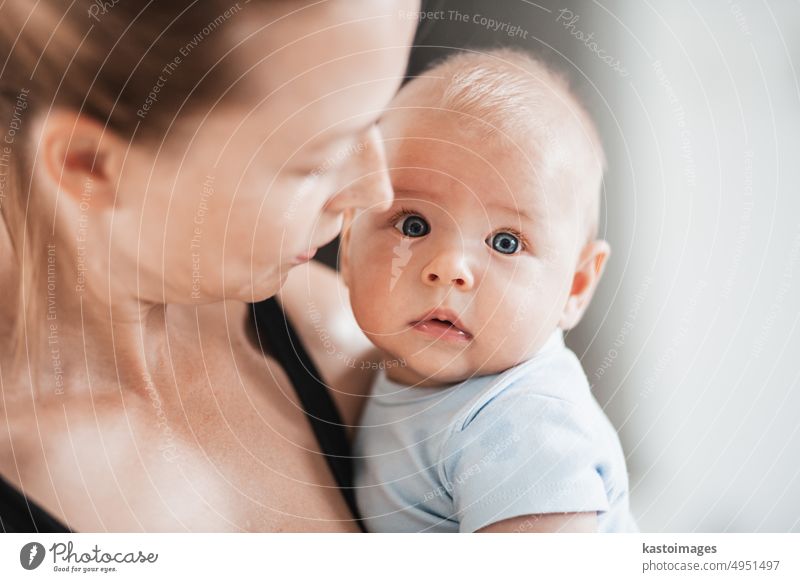 Portrait of sweet baby resting in mothers arms, looking at camera. New mom holding and cuddling little kid, embracing child with tenderness, love, care. Motherhood concept.