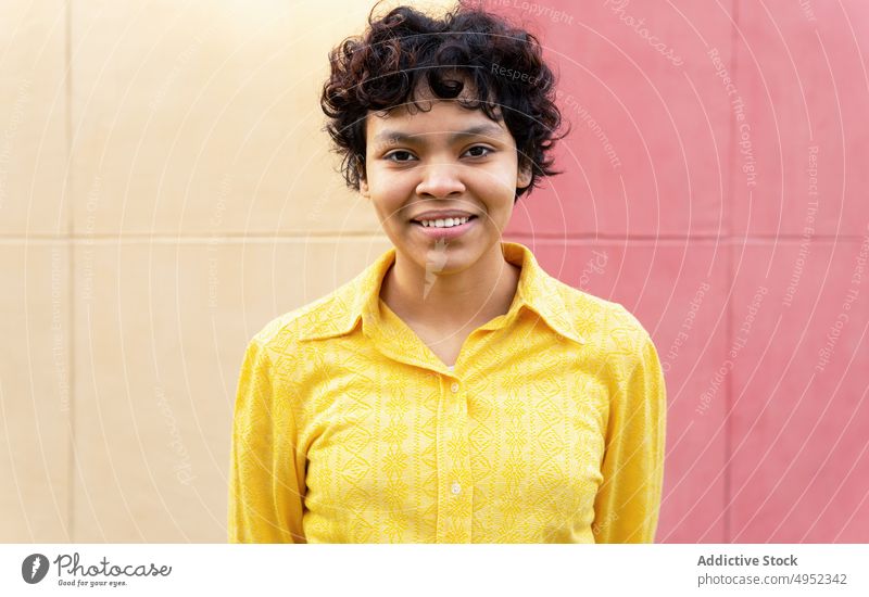 Happy ethnic woman looking at camera on colorful wall cheerful smile bright vivid casual vibrant individuality glad satisfied expressive cover face style