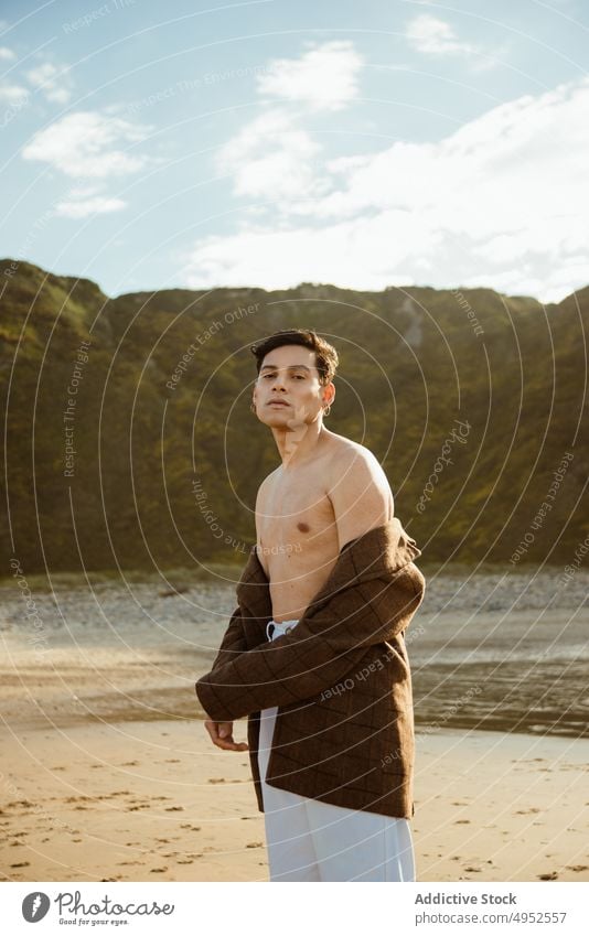 Trendy ethnic guy adjusting jacket on beach man style summer rest sea cliff sunny male model young relax coast shore trendy ocean vacation holiday travel trip